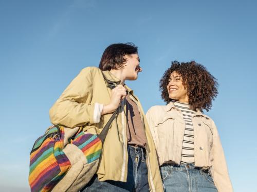 A young couple smiling at each other against a blue sky.