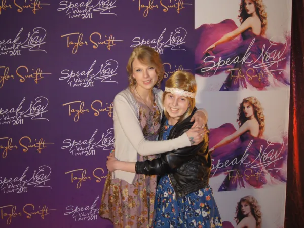 A young girl with blonde hair and a big smile is hugging Taylor Swift
