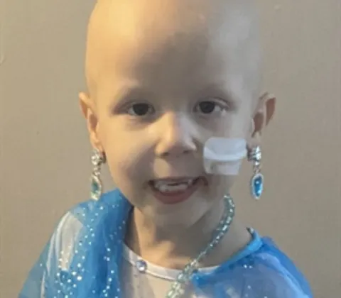 A young girl with a nasogastric tube is smiling at the camera while wearing a blue princess costume.