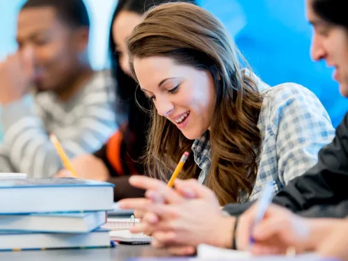 Smiling young people sitting at a table with books and pencils.
